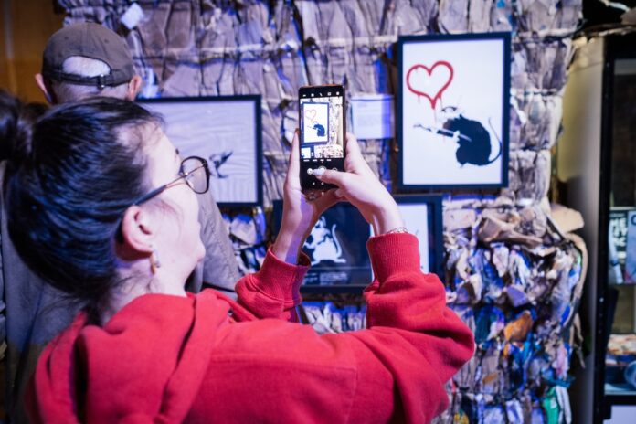 Berchtesgaden: Banksy Modeste Collection zeigt Street-Art Banksy Motiv Besucherin fotografiert Kunstwerk Quelle: @HL_llumineau__ (Bergerlebnis Berchtesgaden)